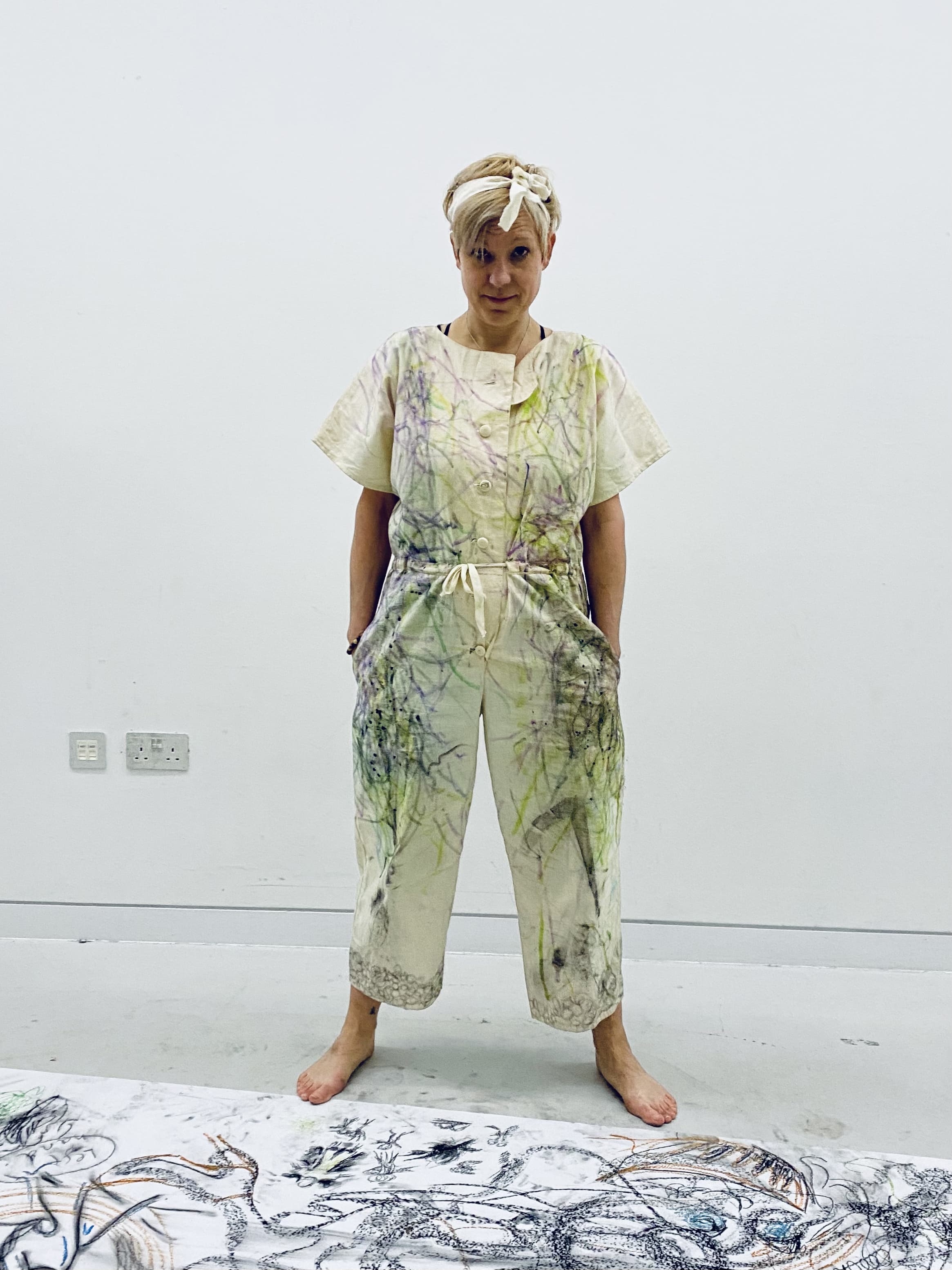 Women in cream jumpsuit with felt-tip and charcoal marks on. Paper with Artistic mark-making on flooe.