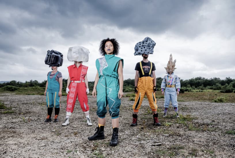 Image of 5 people all with bright jumpsuit style costumes. 4 of the people have large headresses representing rocks (chalk, Coal, Quarts, Igneous)