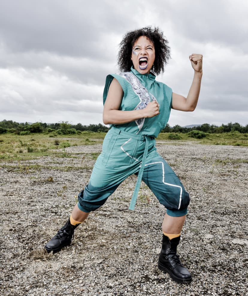 Image if a person a powerful pose wearing a green jumpsuit, outdoors in gravel ground.