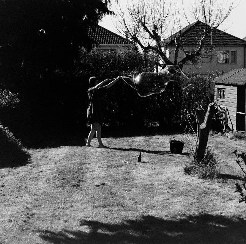 Black and white photo of a person in a garden creating a large soap bubble.